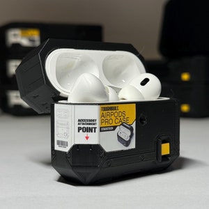 May include: Black protective case for Apple AirPods Pro with a yellow label that reads "Toughbuilt. Airpods Pro Case. Stacktech. Accessory Attachment Point."
