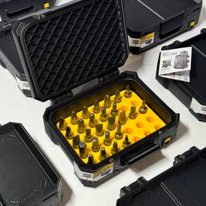 May include: Black toolboxes with yellow interiors and various metal bits. The open toolbox displays an organized array of bits, while others are closed. The text "TOOL BOX" is visible on the side of the box.