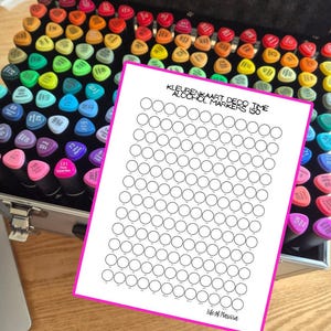 Op de afbeelding: Een grote set alcoholmarkers in een zilveren koffer met een breed spectrum aan gekleurde doppen. Een witte papieren kleurenkaart met de tekst KLEURENKAART DECO TIME ALCOHOL MARKERS 150 en Life of Marissa ligt bovenop de markers.