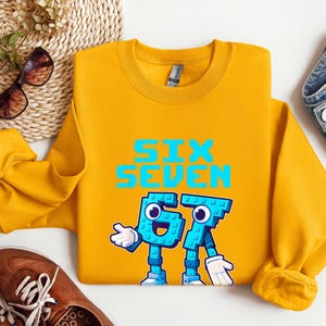 a yellow sweatshirt with a graphic design, a pair of jeans, sunglasses, and a pair of brown shoes, all laid out on a white background.
