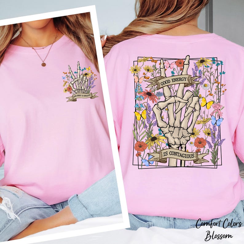 A woman wearing a pink t-shirt with a graphic design on the back, including a skeleton hand and flowers, along with the text "GOOD ENERGY IS CONTAGIOUS" and "Comfort Colors Blossom".