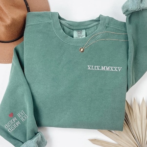 a green sweatshirt with the text "XXI.XXI" printed on it, along with a brown hat and some dried leaves.
