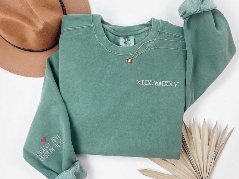 a green sweatshirt with the text "XXI.XXI" printed on it, along with a brown hat and some dried leaves.
