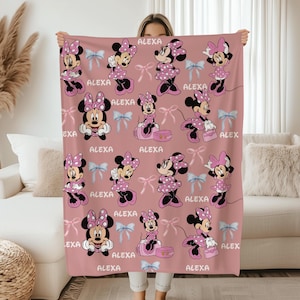 May include: A pink blanket featuring multiple Minnie Mouse illustrations in various poses, wearing polka dot dresses and bows. The name "ALEXA" is printed throughout the design, along with light blue bows. This blanket is perfect for a child's bedroom.