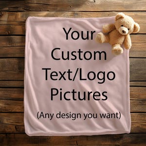 May include: A light pink blanket with the text "Your Custom Text/Logo Pictures" and "(Any design you want)" in black. A small teddy bear is in the upper right corner. The blanket is on a wooden surface.