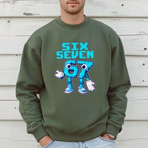 A man wearing a green sweatshirt with a graphic design of a blue robot character and the text "SIX SEVEN" printed on it.