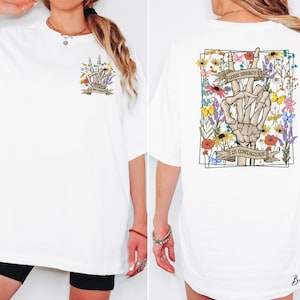 A white t-shirt with a graphic design on the back, featuring a skeleton hand holding a flower and the text "It's Contagious" along with a banner.