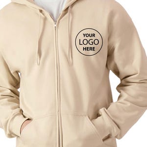 A man wearing a beige hooded sweatshirt with a black logo on the front.