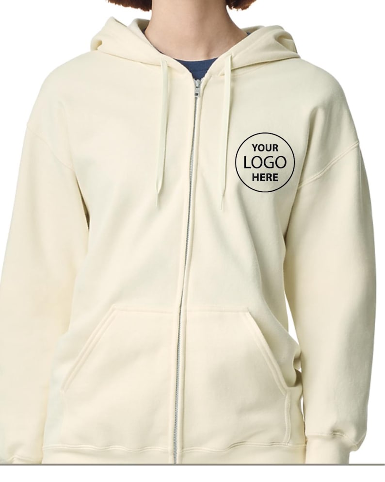 A person wearing a cream-colored zip-up hoodie with a black logo on the front.
