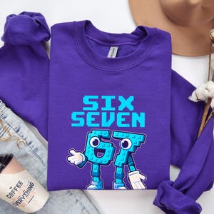 a purple long-sleeved shirt with a graphic design, a pair of jeans, a hat, and some cotton flowers.