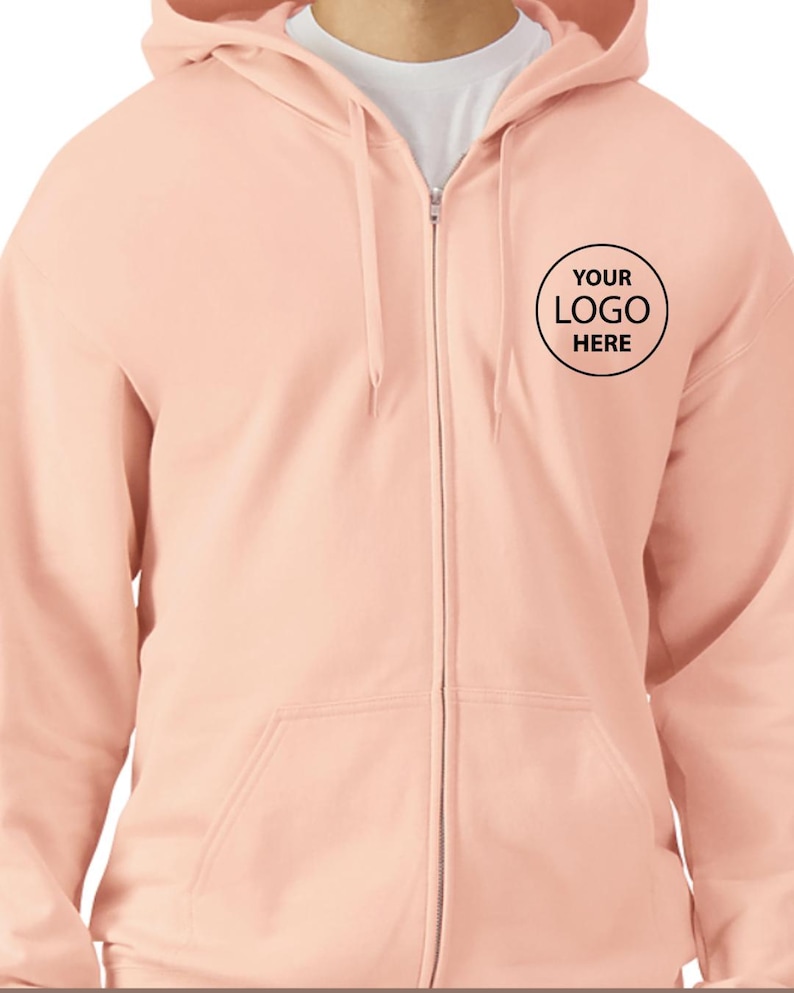 A person wearing a peach-colored hooded sweatshirt with a black logo on the left side of the chest.