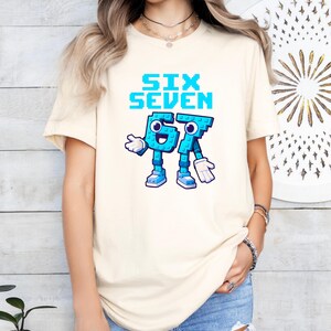 A woman wearing a white t-shirt with a graphic design of a blue character that says "Six Seven" and a number "67" on it.