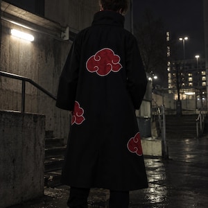 May include: A black, long-sleeved, calf-length coat featuring a high collar and multiple red cloud-shaped appliques with white outlines. The garment is worn over black trousers and white sneakers, displaying a dark, solid color scheme throughout.