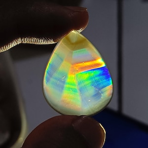 May include: A teardrop-shaped iridescent agate gemstone with a rainbow of colours, including red, orange, yellow, green, blue, and purple.