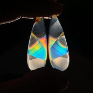May include: Two iridescent agate cabochons with a teardrop shape. The cabochons have a white base with blue, green, and orange iridescent patterns.