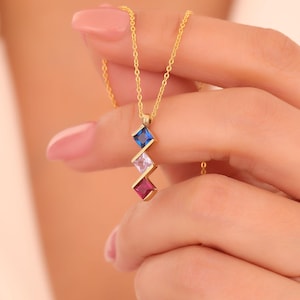 May include: A gold chain necklace with a pendant featuring three square-shaped gemstones: a blue sapphire, a white diamond, and a red ruby.