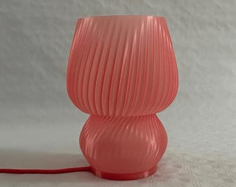 May include: A pink table lamp with a pleated shade and a round base. The lamp has a cord and a plug.