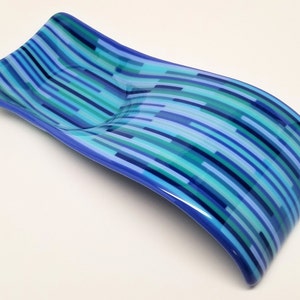 May include: A blue glass dish with a wavy design and a striped pattern in shades of blue, green, and white.