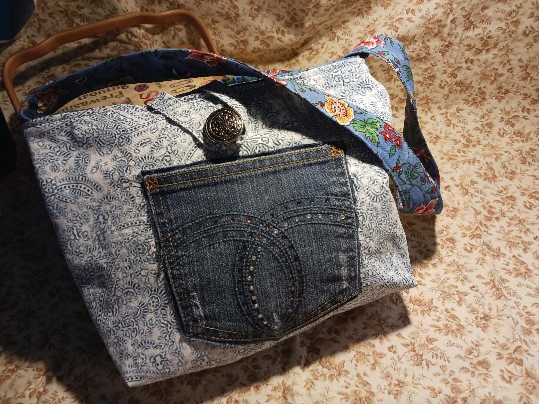Denim print shoulder bag with dazzling jewelled pockets. Button closure. Lined in blue print with 2 interior pockets. wide strap