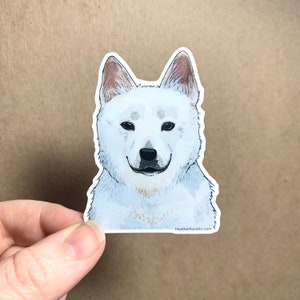 Peut inclure: Autocollant représentant un chien blanc dans un style aquarelle. Le chien a un pelage blanc avec quelques taches brunes et regarde directement le spectateur. L'autocollant a une bordure blanche et le texte "HeatherKentArt.com" est imprimé dans le coin inférieur droit.