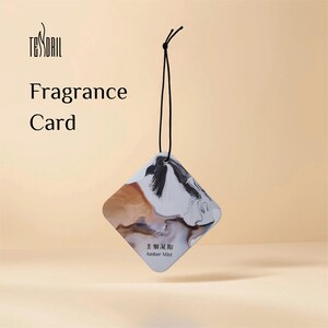 May include: A diamond-shaped fragrance card with a black string for hanging. The card features a marbled design in shades of brown, white, and black. The text "Fragrance Card" is printed on the card, along with the brand name and "Amber Mist".