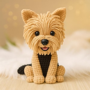 Könnte beinhalten: Gehäkelte Yorkshire Terrier Hundefigur. Der Hund hat hellbraunes Fell, schwarze Augen und eine schwarze Nase. Brust und Rücken des Hundes sind schwarz. Der Hund sitzt mit offenem Mund und zeigt eine rosa Zunge. Die Figur steht auf einer weißen Oberfläche.