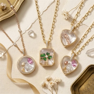 May include: Four gold necklaces with clear glass pendants. One round pendant features a swan and pink stone, one octagonal pendant holds a green four-leaf clover, and two heart-shaped pendants contain swans, pink stones, and small gold flowers.
