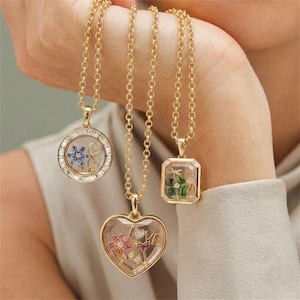 May include: Three gold necklaces with clear floating pendants. One is a round locket with a blue flower, one is a heart-shaped locket with a pink flower and the word LOVE, and one is a rectangular locket with a green four-leaf clover design.