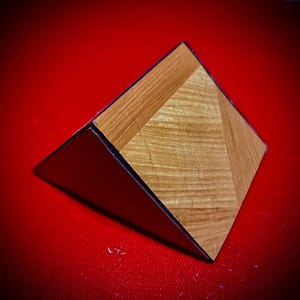 Op de afbeelding: Een driehoekige houten displaystandaard met een zwarte rand. De standaard heeft een houtnerfpatroon en is gemaakt van lichtbruin hout.