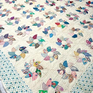 May include: A quilt featuring a repeating pinwheel pattern made from various multicolored fabric scraps. The pinwheels are set against an off-white background with quilted stitching. The border consists of a blue and white floral fabric print.