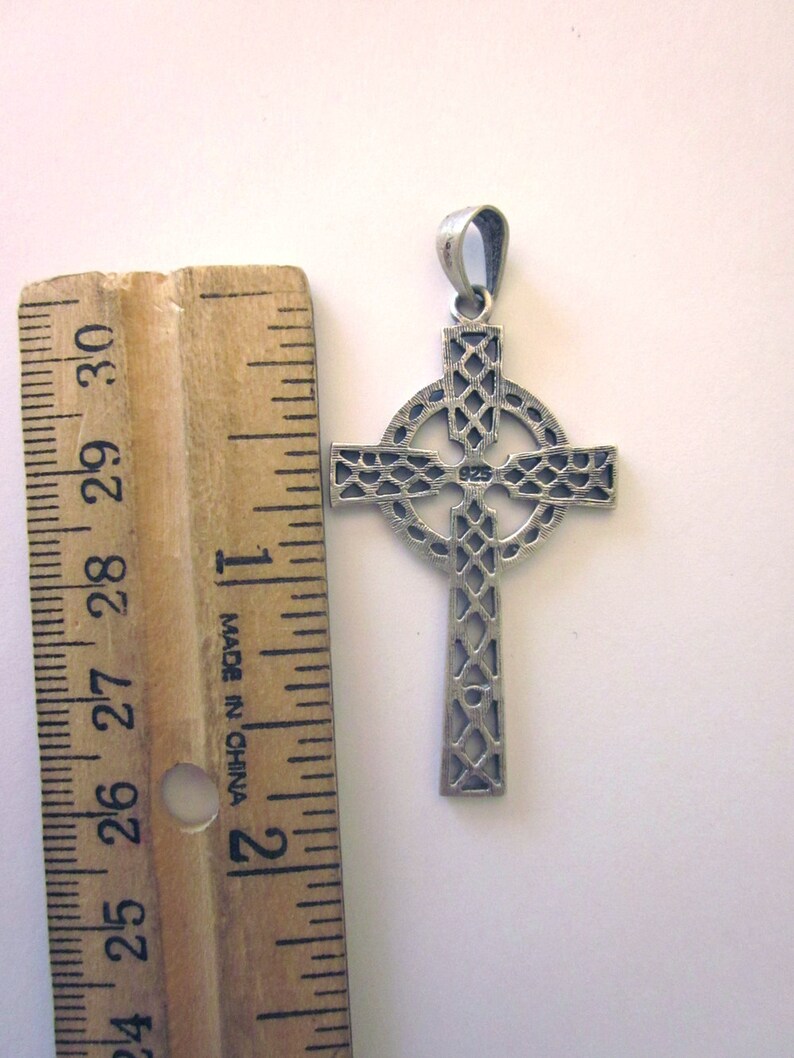 May include: A silver Celtic cross pendant with a detailed, intricate design. The pendant is approximately 1 inch in size and has a bail for attaching to a chain.