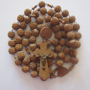 May include: A vintage rosary with intricately carved wooden beads in a warm brown hue. The rosary features a wooden cross with a metal crucifix and a circular pendant. The beads are connected by a dark chain.