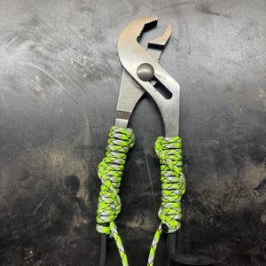 May include: Silver pliers with black handles wrapped in green and white paracord.