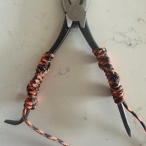 May include: Black pliers with orange and black paracord wrapped around the handles.