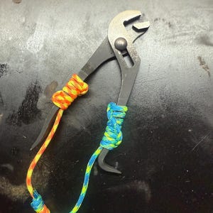 May include: Black pliers with a blue, yellow and orange paracord wrap.