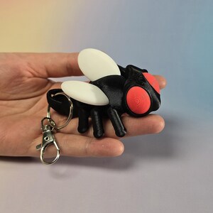 Gelenk Flexi Fly Schlüsselanhänger: Schwarzes Insekt Fidget Spielzeug mit roten Augen