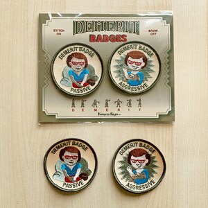 May include: Four embroidered iron-on patches with a cartoon woman wearing glasses and a red shirt. The patches are beige with green and brown accents. The text on the patches reads "Demerit Badge" and "Passive" or "Aggressive".