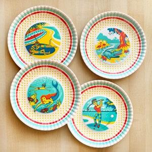 May include: Four colorful plates with a white background and yellow polka dots. Each plate features a different illustration: a mermaid, a golfer, a couple on a beach, and a crocodile in a tropical scene.