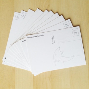 May include: A stack of white postcards fanned out, featuring the text "Wonders of Wisconsin" and a bear illustration. Each card has a space for a stamp and a blank area for a message.