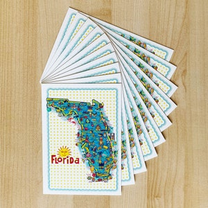 May include: A stack of colorful postcards featuring a map of Florida with the text "Visit Florida" and a sun graphic. The postcards are decorated with a blue and white polka dot pattern.