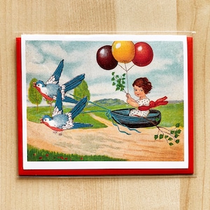 May include: A red, white, and blue card with a girl in a boat being pulled by three blue birds. The girl is holding a string attached to three balloons: one red, one yellow, and one dark blue.