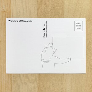 May include: A white postcard with the text "Wonders of Wisconsin" at the top. A black and white illustration of a bear holding a blank rectangle is on the card. The text "Keep the Faye" and a website address are also printed on the card.