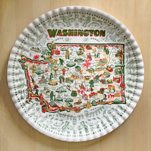 May include: A circular serving tray with a frilled edge. It displays a detailed map of Washington state in red, green, and yellow, with the state name in large letters. The border has a repeating pattern of illustrations.