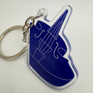 Peut inclure: Un porte-clés en acrylique transparent présentant une forme découpée bleu foncé d'une contrebasse. L'instrument est souligné par de fines lignes blanches, montrant le manche, le corps et les ouïes. Un anneau en métal argenté est fixé au sommet.