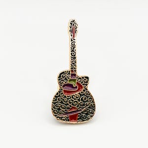 Peut inclure: Une épingle en émail en forme de guitare dorée avec un motif de tourbillon noir. L'épingle présente des accents rouges, violets, verts et dorés. La tête et le corps de la guitare sont ornés de motifs complexes.