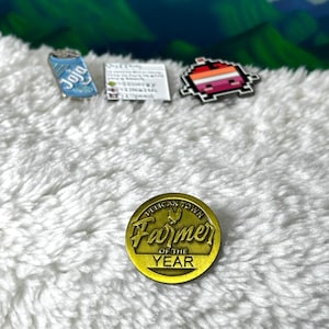 May include: Gold-colored pin with the text "Pelican Town Farmer of the Year" and a stylized chicken design.