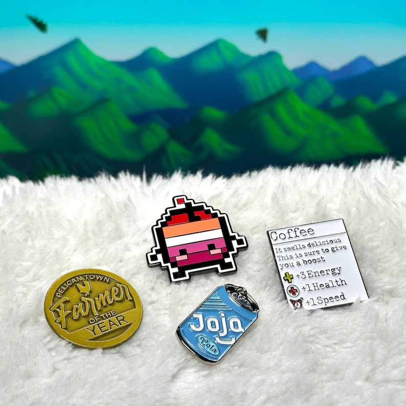 May include: Four enamel pins featuring a pixelated character, a can of Joja Cola, a gold pin with the text "Pelican Town Farmer of the Year", and a white card with the text "Coffee It smells delicious This is sure to give you a boost +3 Energy +1 Health +1 Speed"