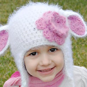 May include: A white crocheted hat with fuzzy white yarn and pink ears. The hat has a pink flower on top and a pink scarf around the neck.