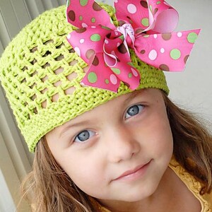 May include: A young girl wearing a lime green crocheted hat with a pink and green polka dot bow. The hat has a crocheted design with open spaces.