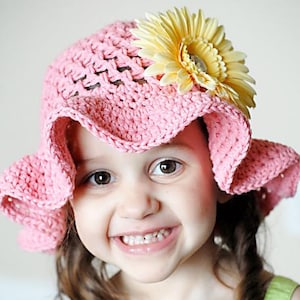 May include: A young girl wearing a pink crocheted sun hat with a yellow flower accent. She is smiling with her teeth showing.